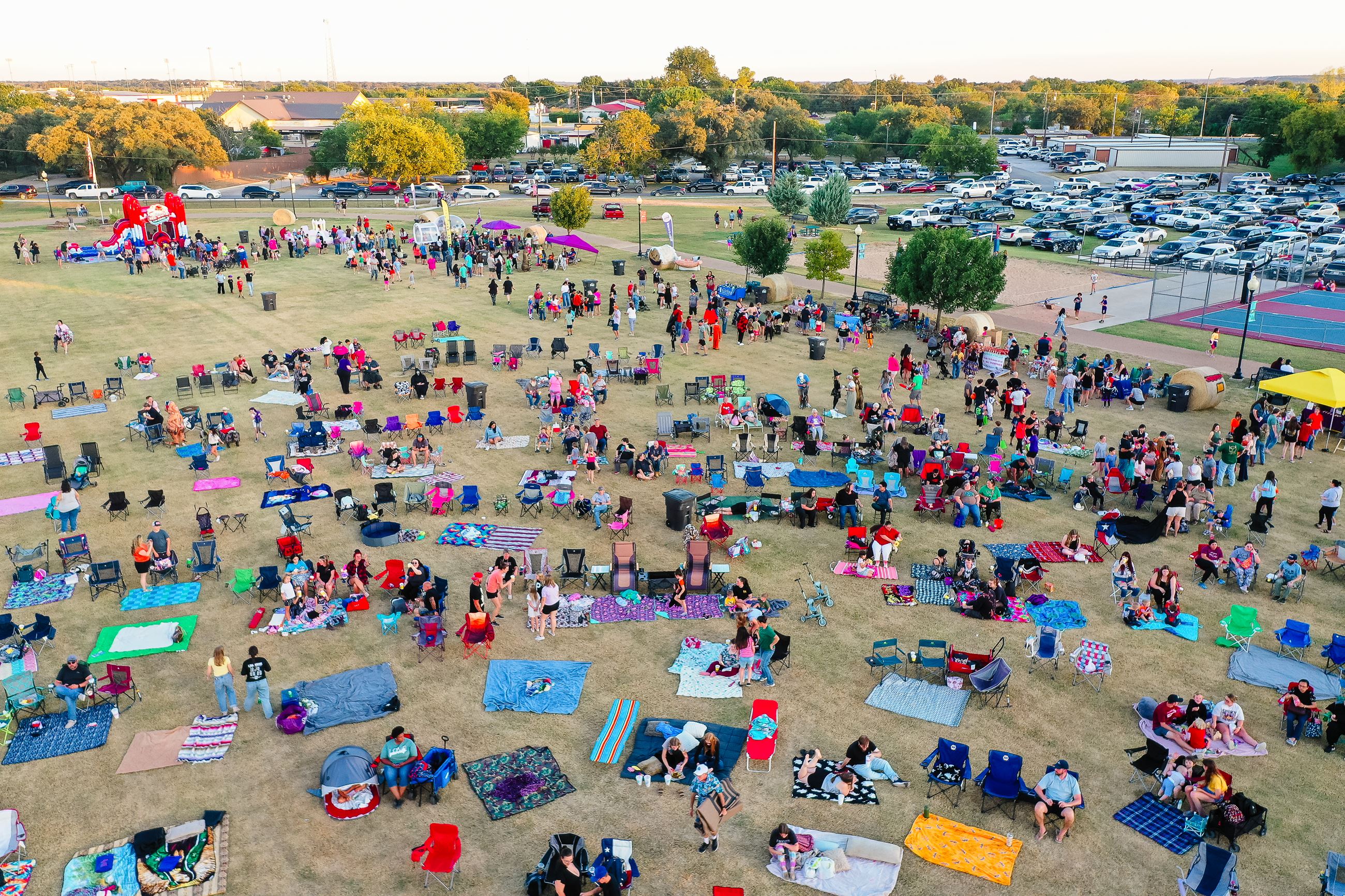 Drone pictures of over 500 people sitting down in a grassy open park with blankets